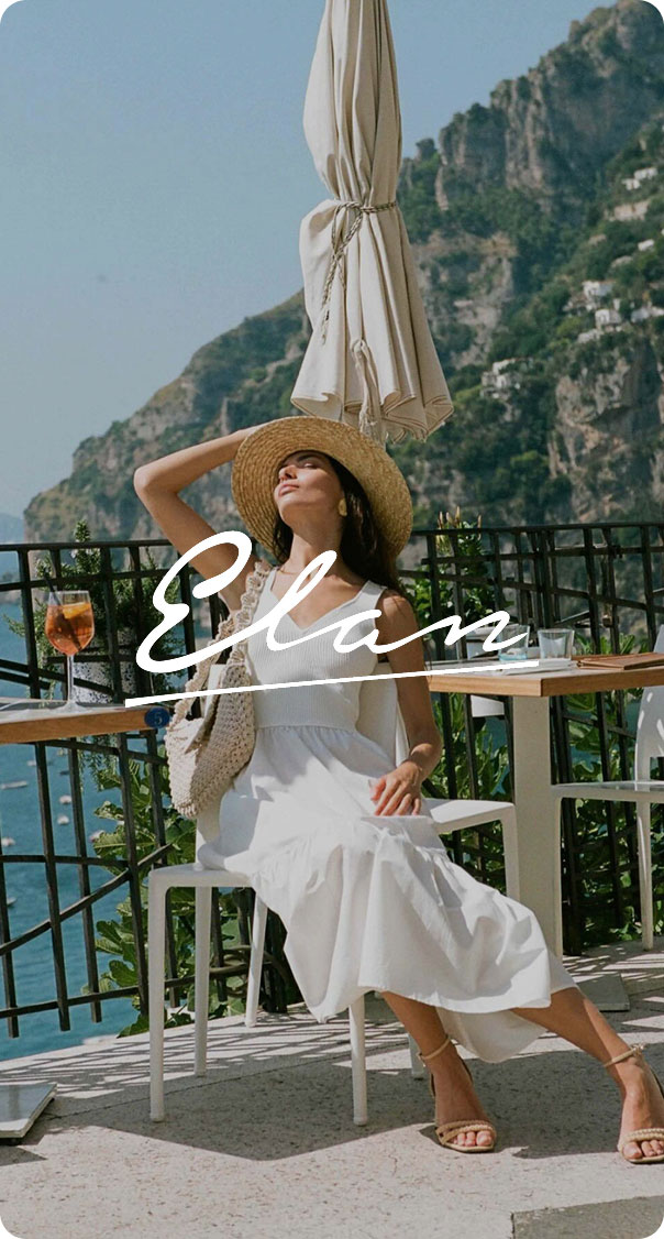 woman in white summer dress and straw hat sitting on terrace overlooking the sea