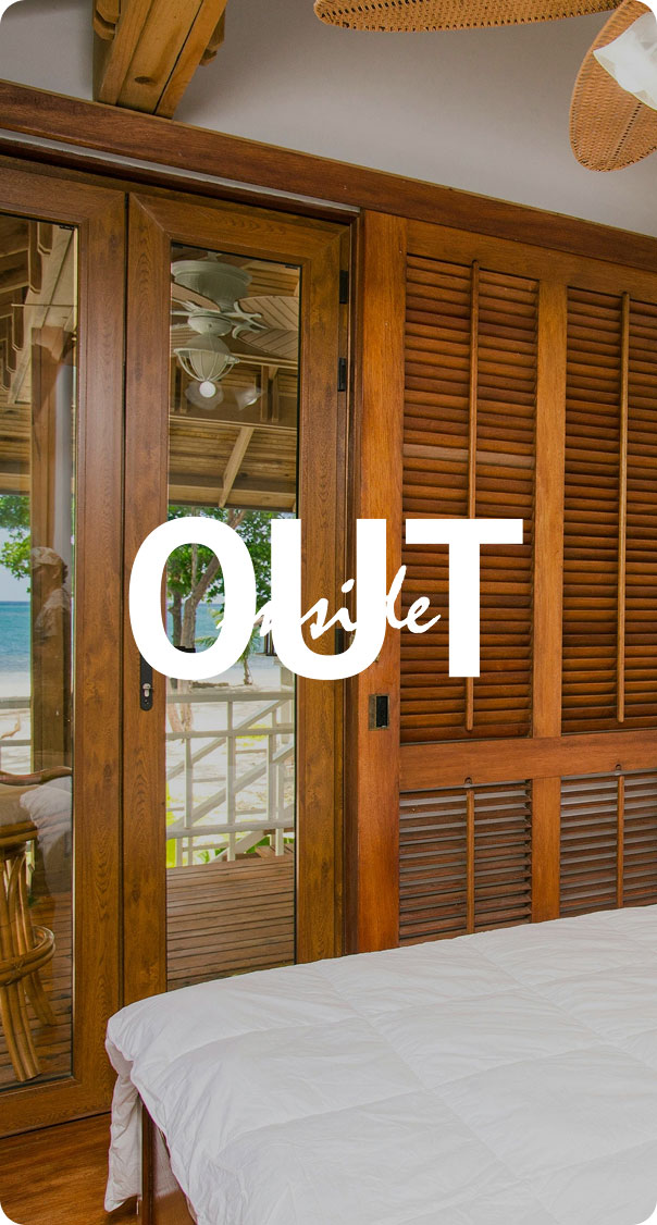 tropical bedroom with wooden doors opening to balcony and ocean view