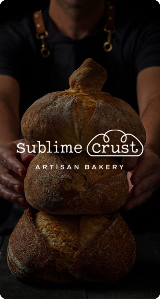 artisan baker holding stacked rustic bread loaves in a dark setting, featured in a bakery branding project by a miami web design company